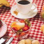Delicious breakfast table with coffee, fresh fruits, and bread on a checkered tablecloth.