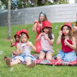 Group of children and adults blowing bubbles in a sunny park setting.